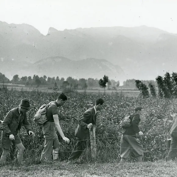 Sechs Männer laufen in einer Reihe an einem Feld entlang