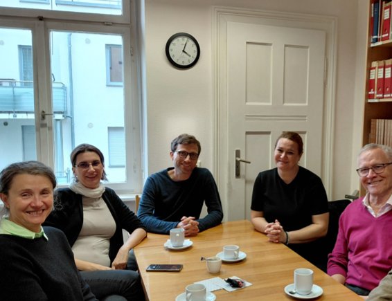 Drei Frauen und drei Männer sitzen an einem Tisch und blicken in die Kamera. Auf dem Tisch stehen Kaffeetassen.