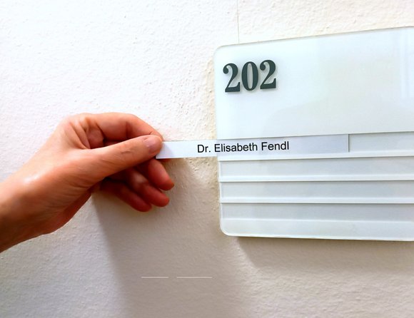 Eine Hand zeiht an einen Namenschild 