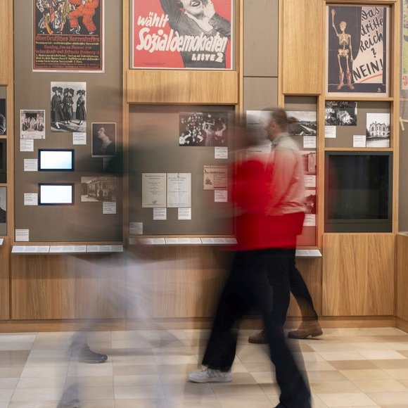 Mehrere Personen in einem Ausstellungsraum im Museum. An den Wänden hängen Fotografien.