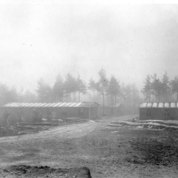 Eine Lagerunterkunft in einem Wald. Es ist neblig und auf dem Boden sowie auf dem Dach des Lagers befindet sich Frost.
