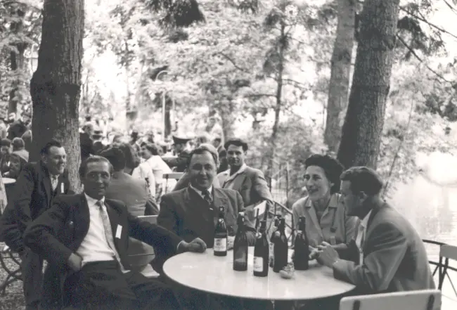 In einem Biergarten sitzen drei Männer und eine Frau an einem runden Tisch.