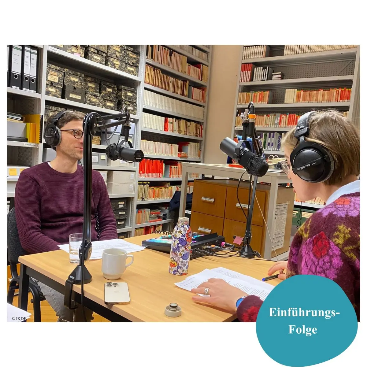 Ein Mann sitzt einer Frau an einem Tisch gegenüber. Beide tragen Kopfhörer und sprechen in Mikrofone.