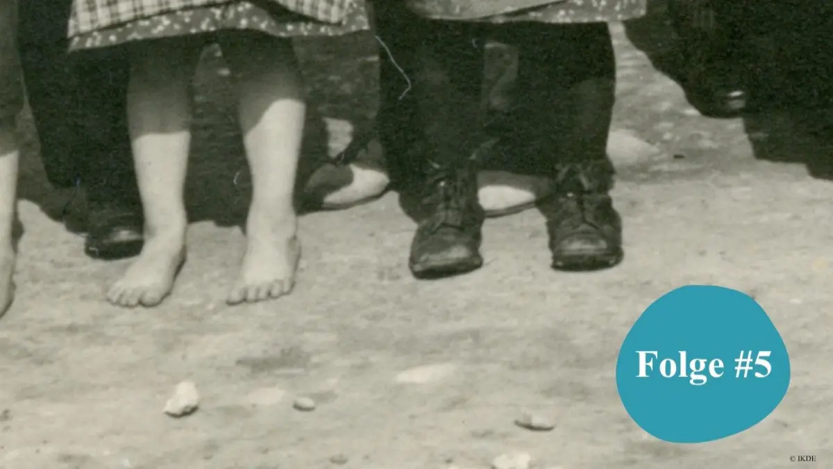 Detail von Kinderfüßen: Das Mädchen ist barfuß, der Junge trägt eine lange Hose und schwarze Schuhe.