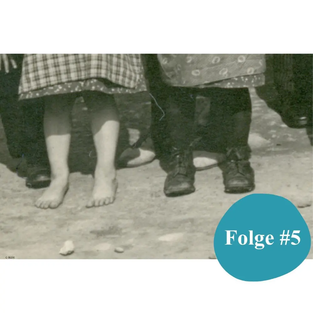 Detail von Kinderfüßen: Das Mädchen ist barfuß, der Junge trägt eine lange Hose und schwarze Schuhe.