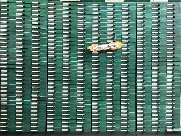 An einem Regal mit grünen Schubern hängt ein kleines Schild mit der Aufschrift "Sagenarchiv"