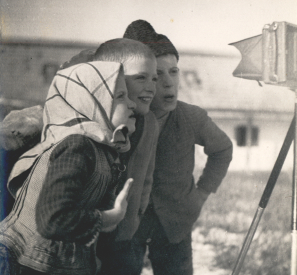 Drei Kinder stehen hinter einer Kamera auf einem Stativ und schauen durch den Sucher.