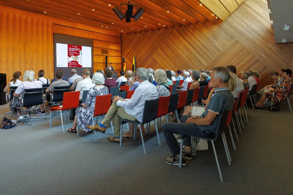 Viele Leute sitzen in einem Saal und hören einem Redner zu.