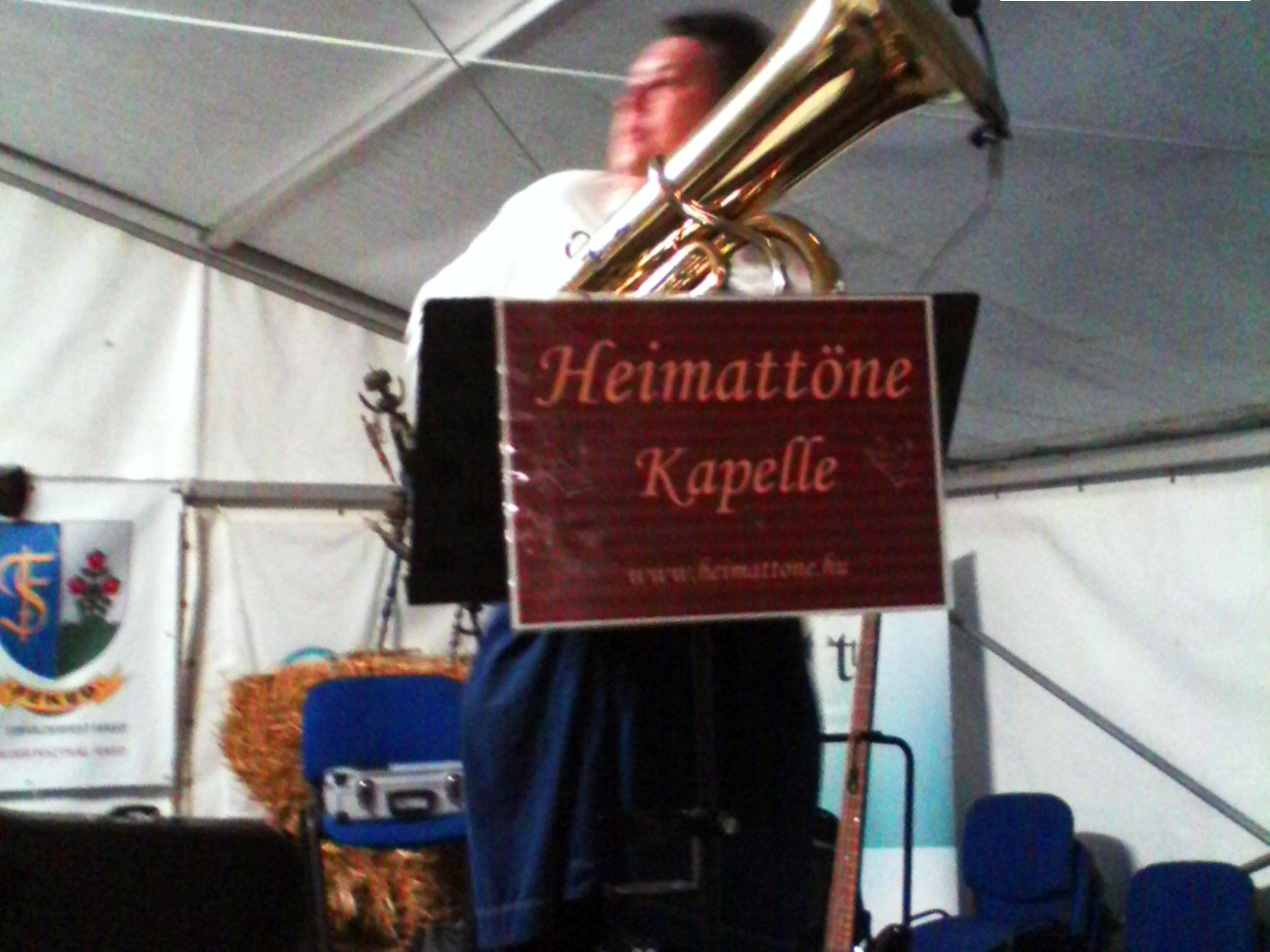 Ein Mann mit einer Tuba in den Händen, davor ein Schild mit der Aufschrift "Heimattöne Kapelle."