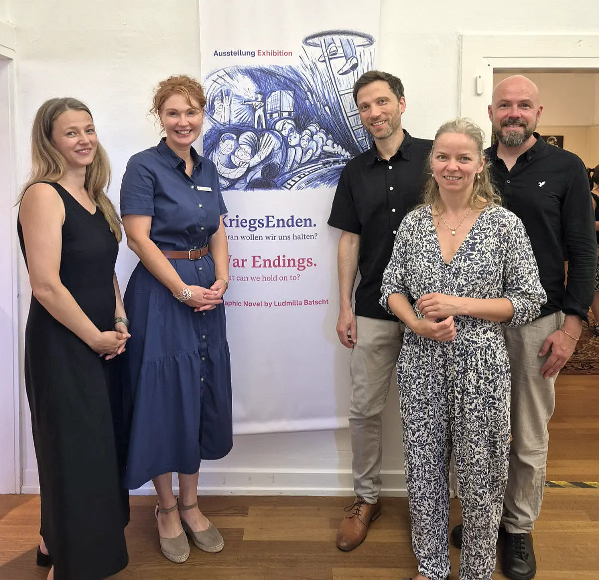 Gruppenfoto von fünf Personen vor dem Banner der Ausstellung „KriegsEnden“. Die Aufnahme entstand in den Ausstellungsräumen.