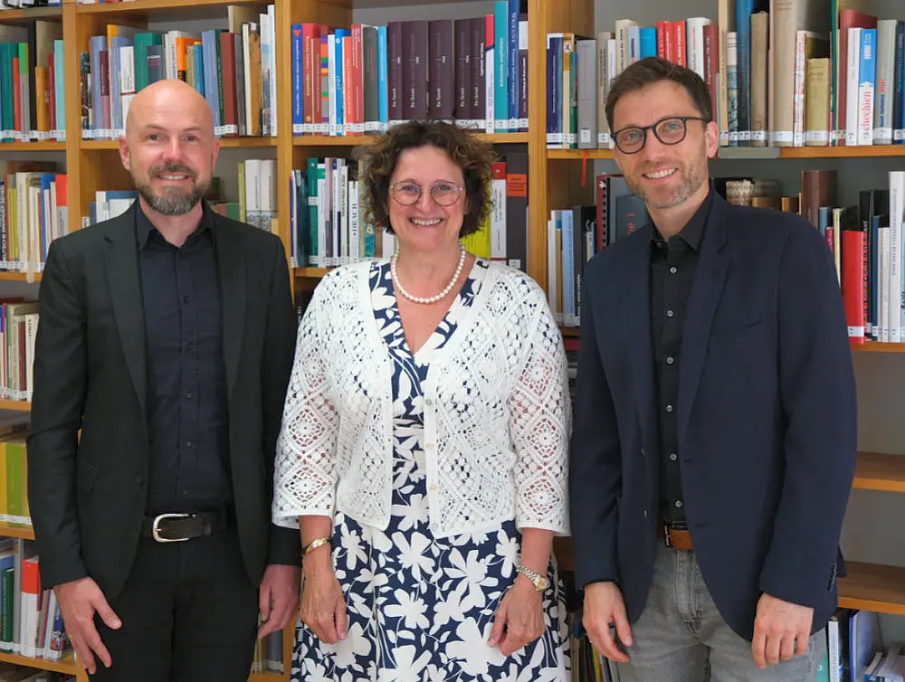 Zwei Männer und eine Frau stehen vor einem Bücherregal