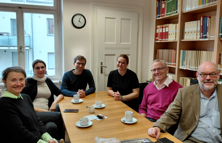 Drei Frauen und drei Männer sitzen an einem Tisch und blicken in die Kamera. Auf dem Tisch stehen Kaffeetassen.