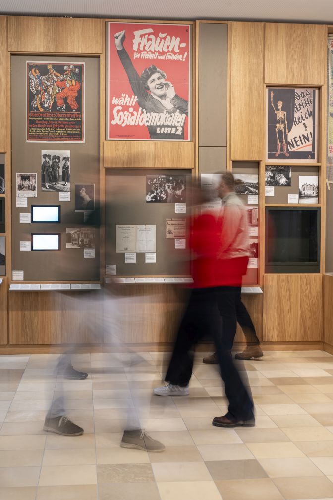 Mehrere Personen in einem Ausstellungsraum im Museum. An den Wänden hängen Fotografien.